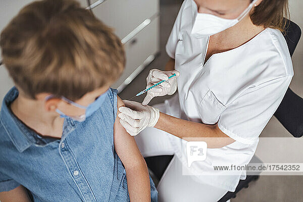 Nurse in protective face mask administering boy with COVID-19 vaccine