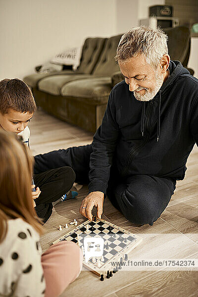 Smiling grandfather playing chess with grandchildren at home