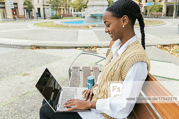 Glückliches Mädchen sitzt mit Laptop auf einer Bank im öffentlichen Park