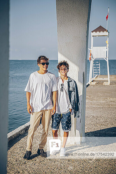 Smiling brothers standing on pier in front of sea
