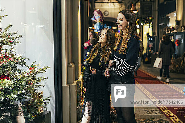 Smiling friends looking at Christmas tree through store window at night