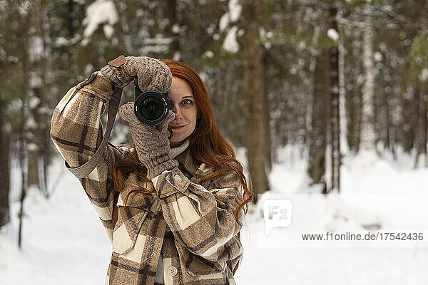 Woman photographing with camera in winter forest