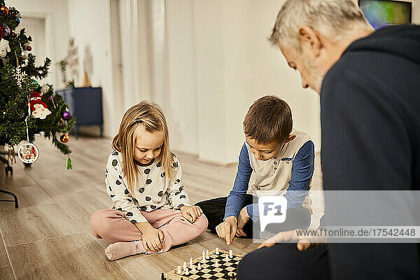 Grandchildren playing chess with grandfather at home