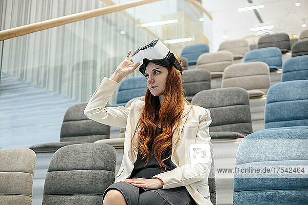 Working woman with virtual reality simulator sitting at office auditorium