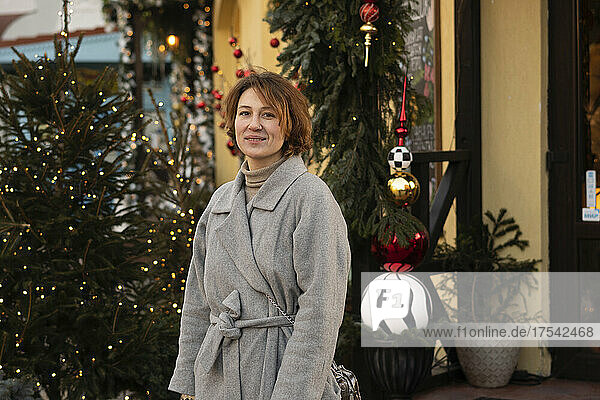 Smiling woman in overcoat standing by christmas trees