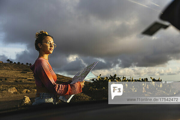 Young woman holding map seen from car windshield at sunset
