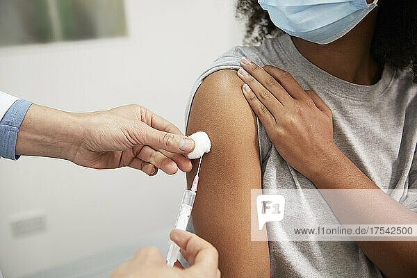 Doctor injecting COVID-19 vaccine through syringe in patient's arm at hospital