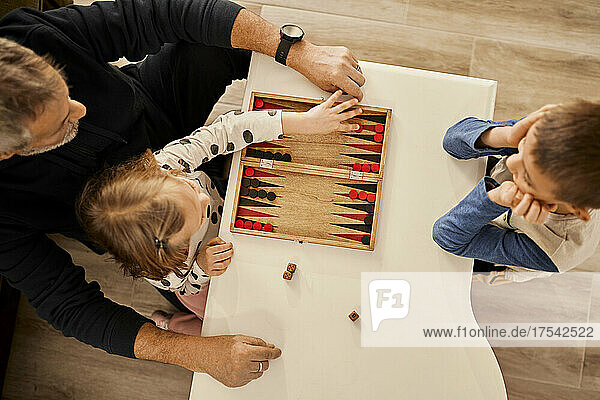 Grandfather playing backgammon on table with grandchildren at home
