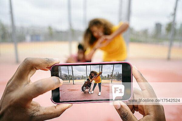 Man photographing friends through smart phone at sports court