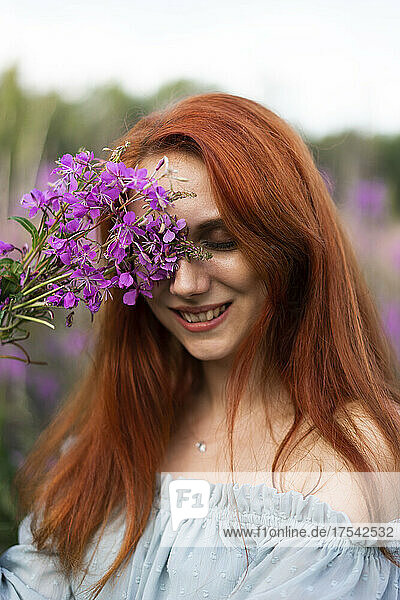 Smiling redhead woman with pink flowers at field