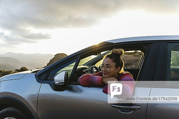 Lächelnde Frau lehnt sich bei Sonnenuntergang aus dem Autofenster