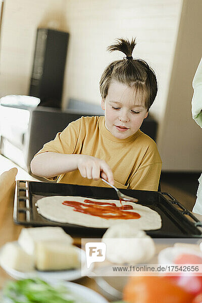 Boy spreading sauce on pizza dough at home