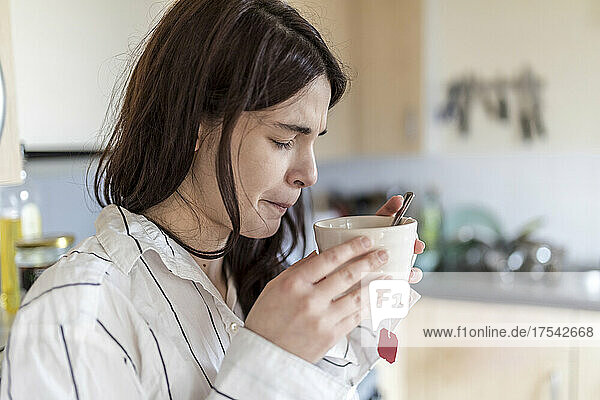 Frau mit geschlossenen Augen trinkt Tee in der heimischen Küche