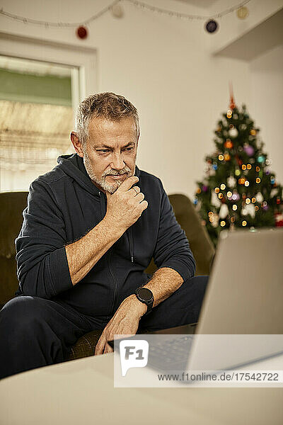 Senior man with hand on chin looking at laptop
