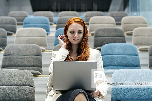 Businesswoman holding laptop sitting with hand in hair at office