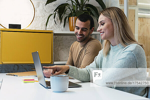 Lächelnder Freiberufler zeigt mit Kollege im Studio auf Laptop