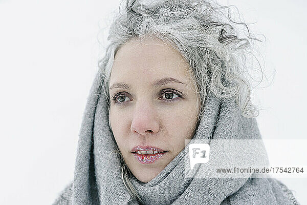 Thoughtful woman with snow on lips wrapped in gray scarf