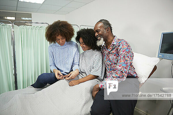 Father and mother sitting with daughter on bed at hospital