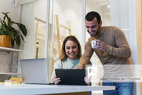 Happy business colleagues sharing tablet PC working at studio
