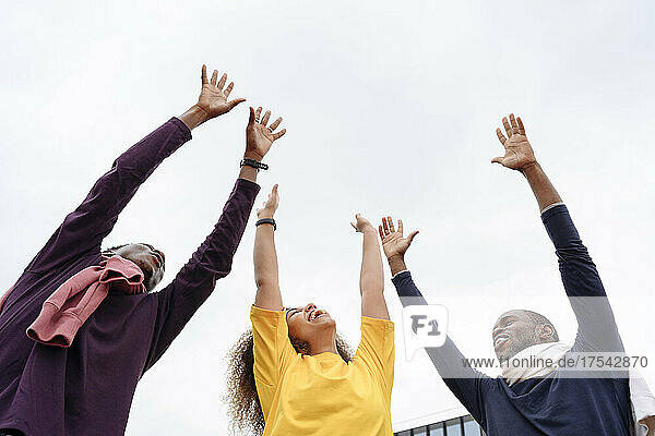Happy friends with hands raised in front of clear sky