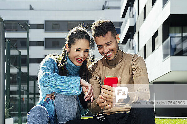 Smiling man sharing smart phone with woman on sunny day