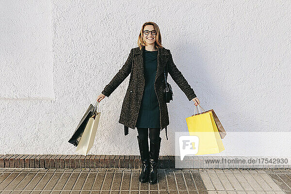 Smiling woman standing in front of white wall holding shopping bags
