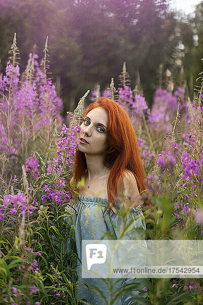 Young redhead woman standing amidst flowering plants in meadow on weekend