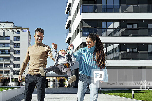Cheerful parents swinging baby boy in city
