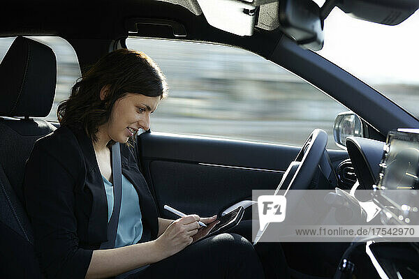 Smiling businesswoman using tablet PC in autonomous driving car