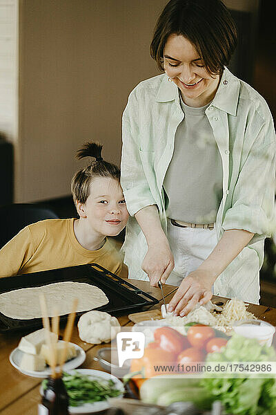 Smiling mother preparing pizza with son at home