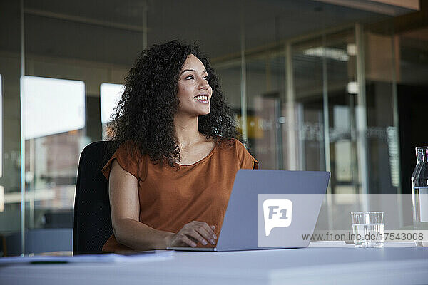 Happy businesswoman with laptop on desk day dreaming in office