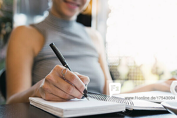 Young businesswoman writing in diary at cafe
