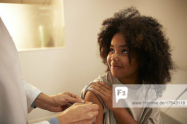 Smiling girl looking at doctor applying adhesive bandage on arm at hospital