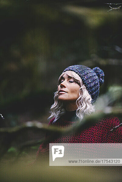 Woman wearing knit hat with eyes closed in forest