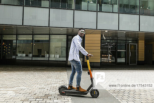 Young man riding electric push scooter on footpath