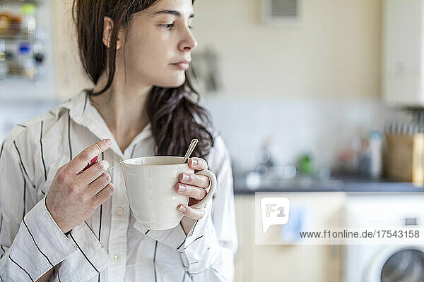 Junge Frau hält Teetasse in der heimischen Küche
