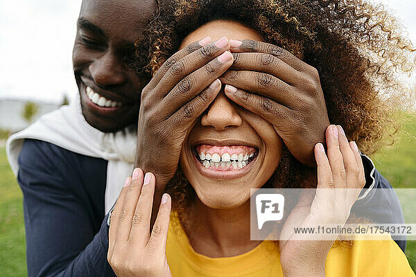 Happy young man covering friend's eyes with hands at park