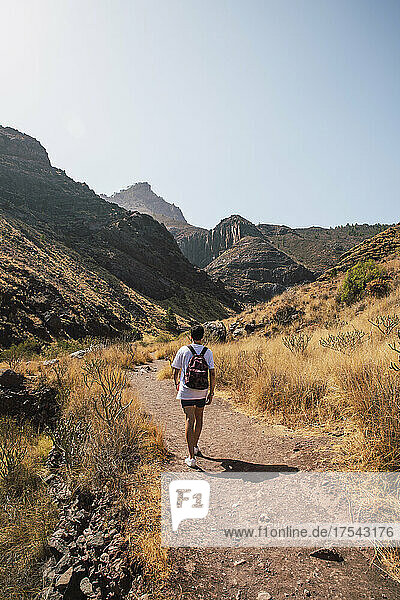 Young man walking on trail towards mountain range  Grand Canary  Canary Islands  Spain