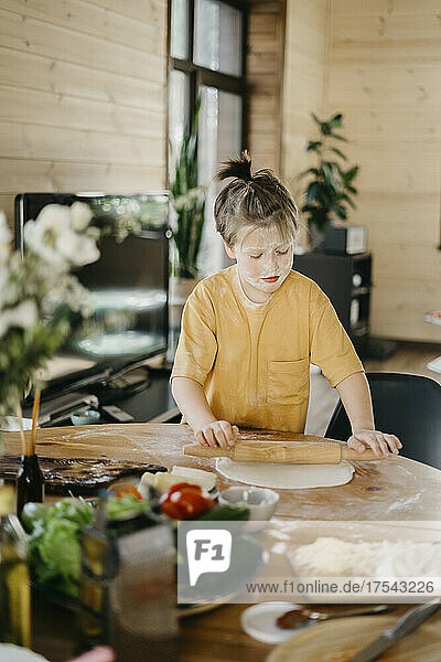 Boy with flour on face flattening dough at home