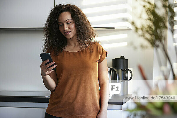 Smiling businesswoman using smart phone in office kitchen