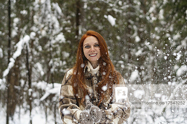 Smiling woman enjoying snowfall in winter forest