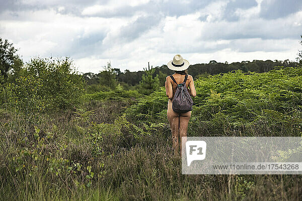 Naked woman with backpack and hat standing in nature at Cannock Chase