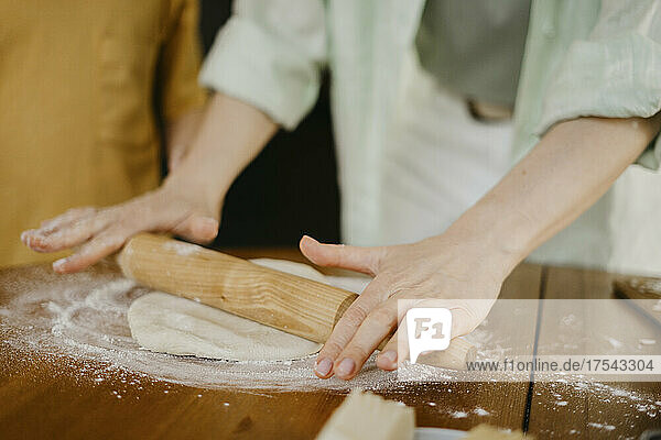 Woman flattening pizza dough with rolling pin on table