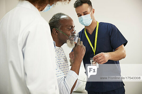 Patient adjusting oxygen mask with healthcare experts in medical room