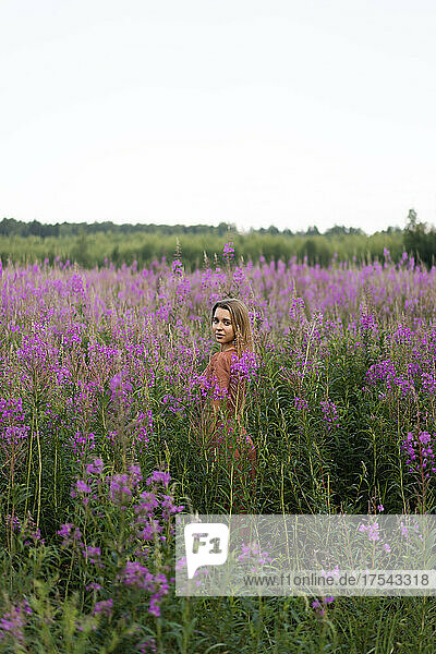 Young woman amidst pink flowering plants in meadow