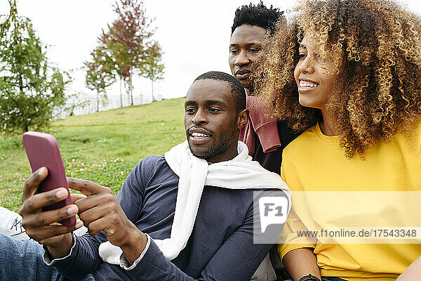 Young man sharing smart phone with friends in park
