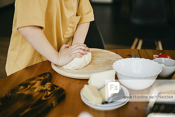 Boy kneading pizza dough on table at home
