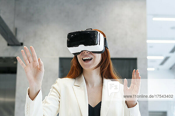 Excited working woman wearing virtual reality simulator gesturing with mouth open at office