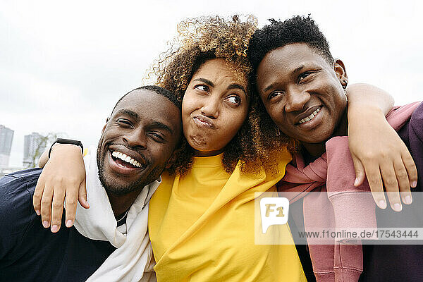 Woman making facial expression with smiling friends in front of clear sky