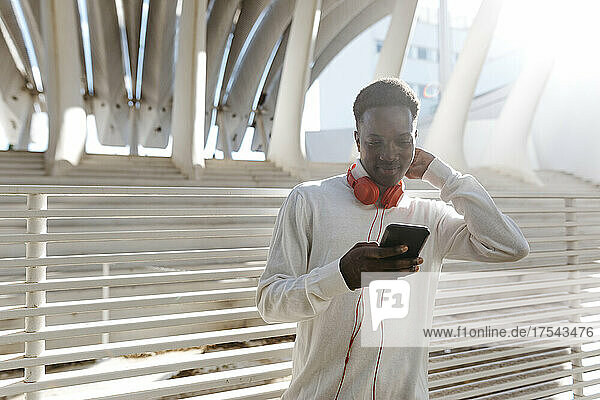 Young man wearing headphones using smart phone on sunny day